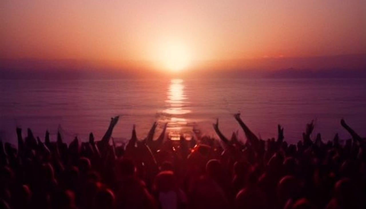 Gente bailando con los brazos en alto frente a la puesta de sol sobre el mar